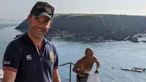 Майк Коннер стоит у моря на фоне острова Торн